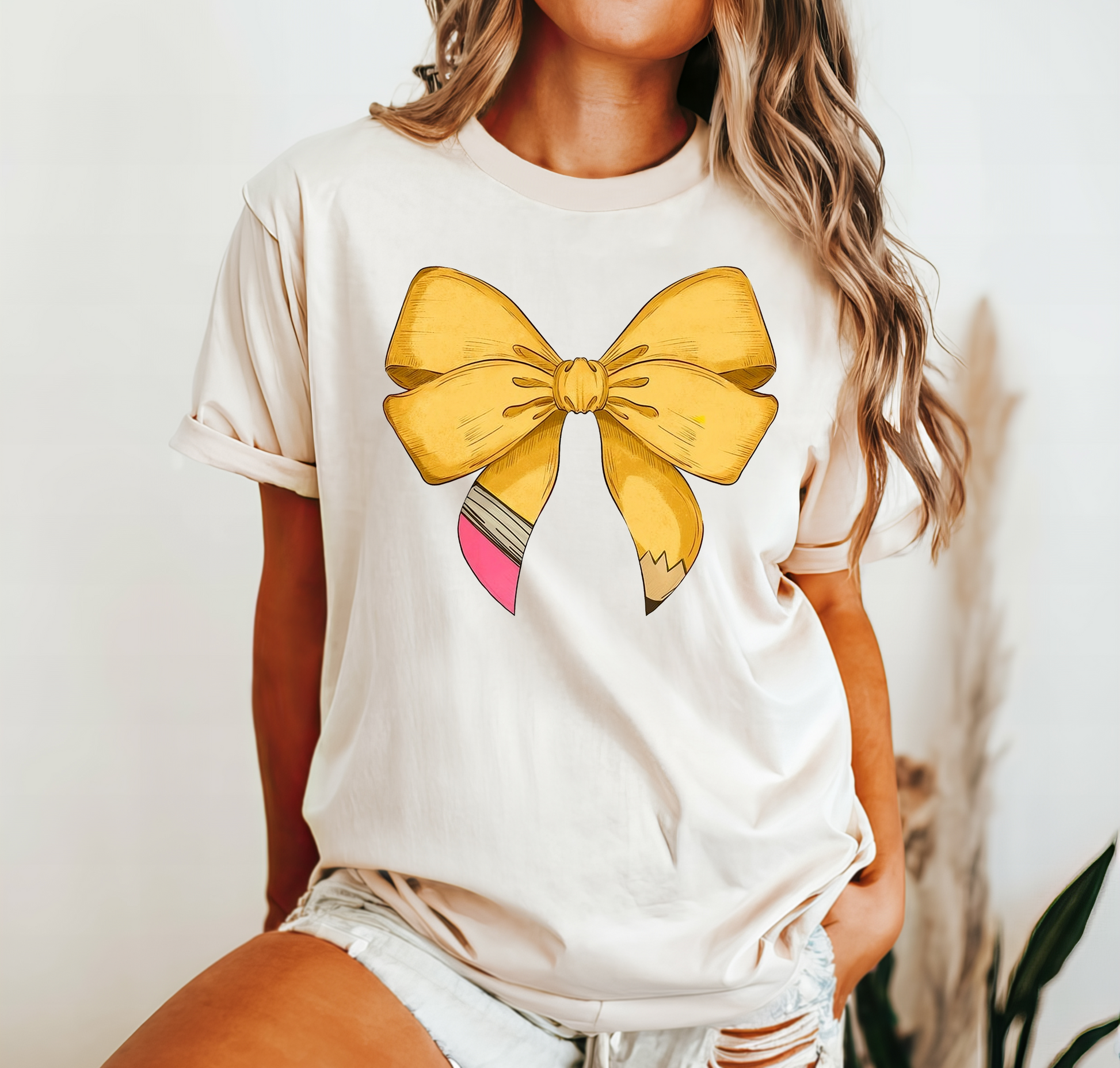 Cream colored t-shirt with a pencil shaped like a bow